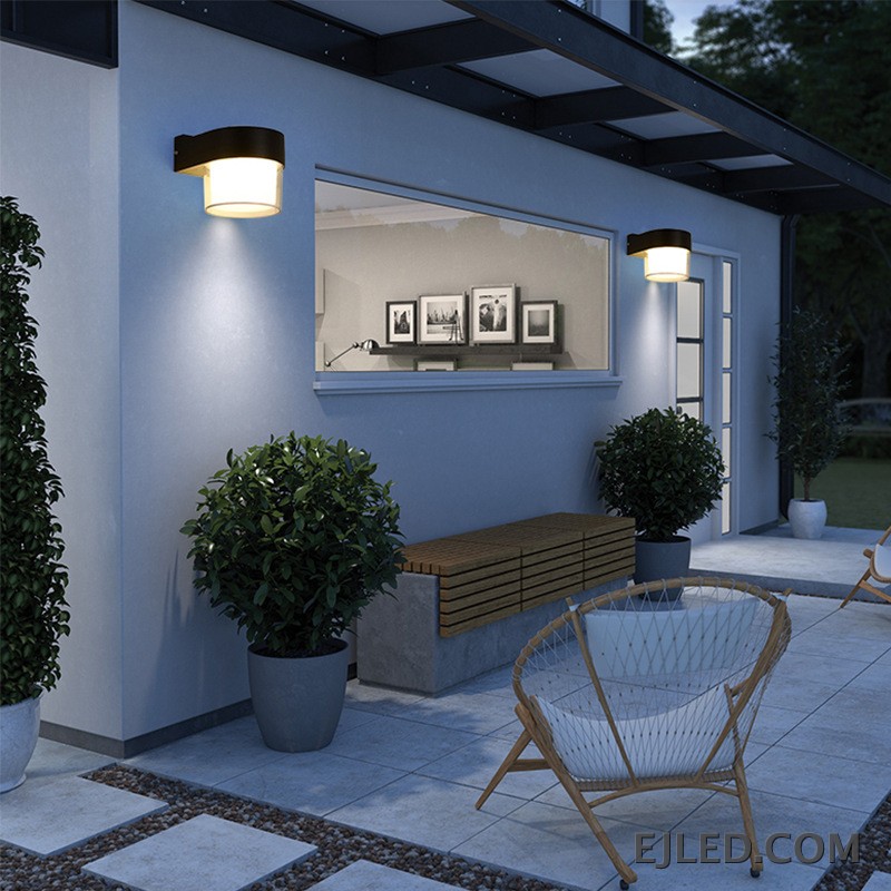 This wall lamp features a textured black plastic body with a curved arm, enclosing a cylindrical light source. It has an inner frosted diffuser and an outer clear enclosure for emitted light. - view 3