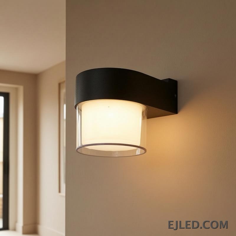 This wall lamp features a textured black plastic body with a curved arm, enclosing a cylindrical light source. It has an inner frosted diffuser and an outer clear enclosure for emitted light. - view 6