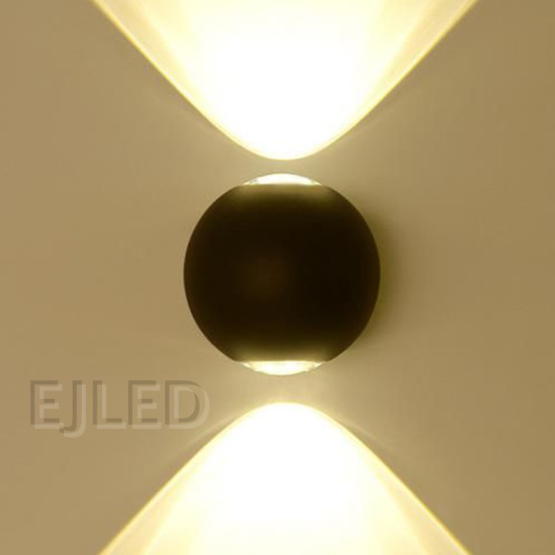 This wall light features a round black acrylic body flanked by two glowing triangular shades that project warm light outward on both sides. - view 4